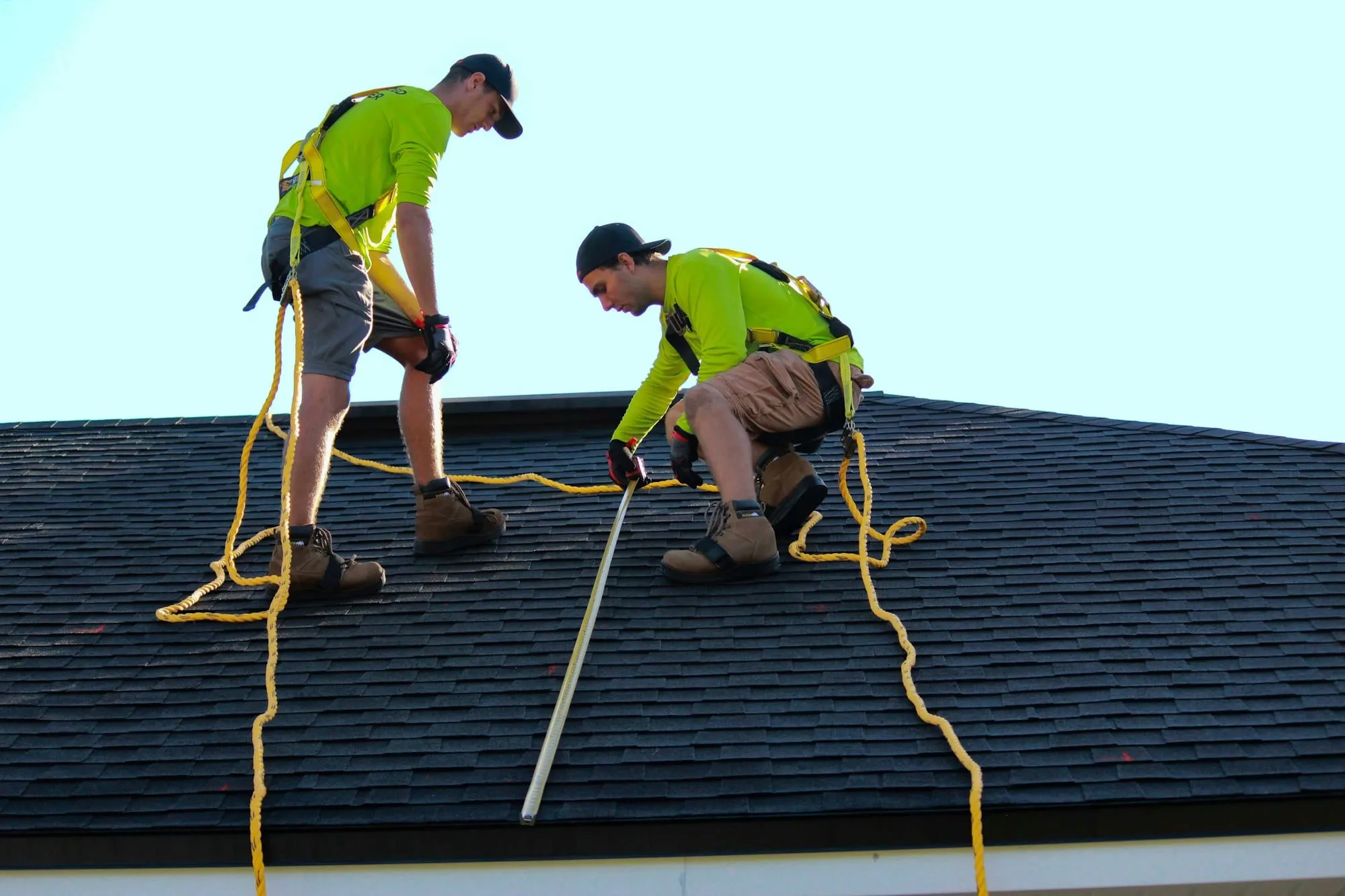 Two roofers in safety harnesses installing shingles