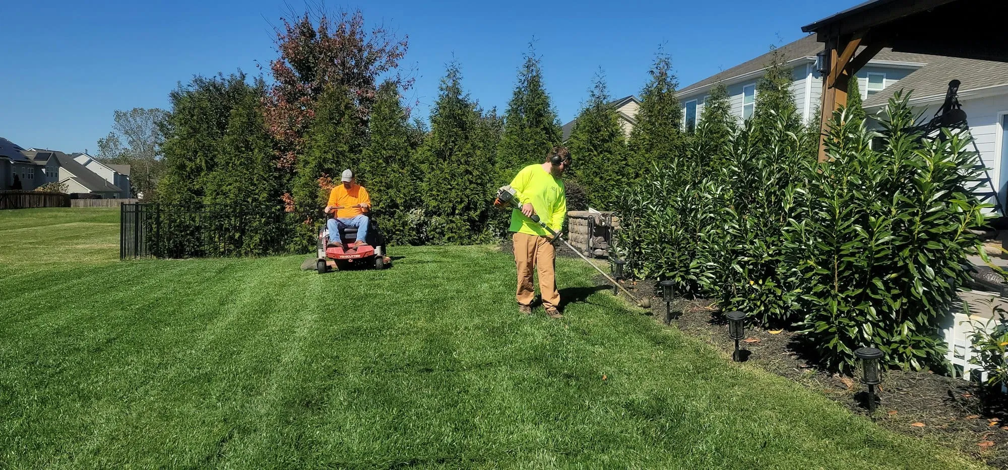 Two landscapers mowing and trimming a lawn